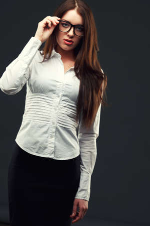 businesswoman wearing glasses over dark background looking at the camera and holding glassesの写真素材