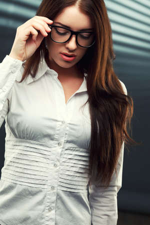 businesswoman wearing glasses in front of a striped background looking down and holding glassesの写真素材