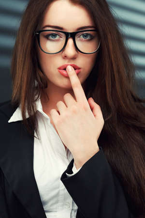 close-up portraits of a business woman on a dark striped background, she holds a finger to her mouthの写真素材