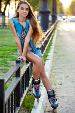 roller skate girl wearing jeans sitting on iron fence over sunsetの写真素材