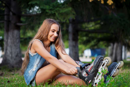 smiling girl sitting on the grass in park and puts on skatesの写真素材