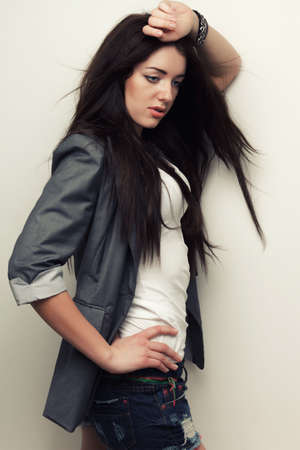 woman fashion studio portrait with flying hair over white wall, holding hand over headの写真素材