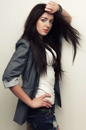 woman fashion studio portrait with flying hair over white wall, holding hand over headの写真素材
