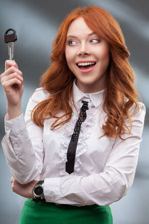 happy red haired woman holding big keyの写真素材