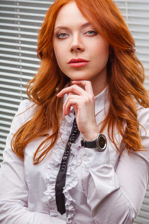 red-haired businesswoman standing over blinds, close up portraitの写真素材