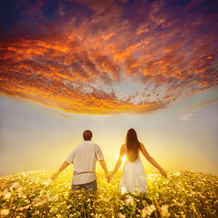 young couple holding hands and walks away into the sunsetの写真素材