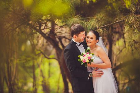 happy bride and groom in conifer trees parkの写真素材