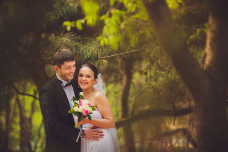 happy bride and groom in conifer trees parkの写真素材