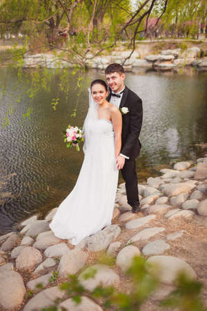 bridal couple standing over lake and stonesの写真素材