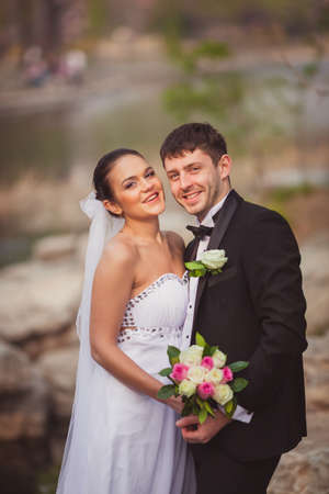 bridal couple standing over lake and stonesの写真素材