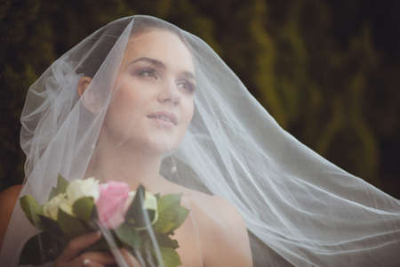 beautiful bride closeup portrait under veil over green trees outdoorの写真素材