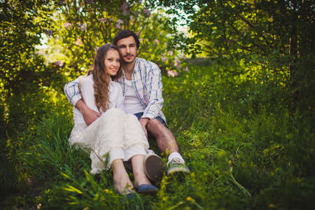 young adult couple in love sitting and hugging at summer parkの写真素材
