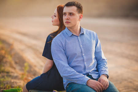 beautiful young couple sitting outdoors back to backの写真素材