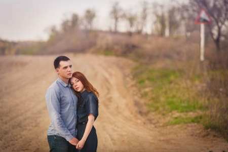 beautiful young couple embracing outdoors holding hands, they stand on the dirt roadの写真素材