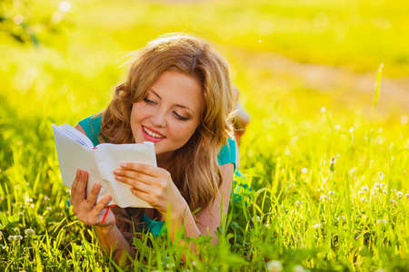 happy woman sitting reading book outdoorsの写真素材