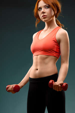 red -haired woman excersising with red dumbbells over color backgroundの写真素材