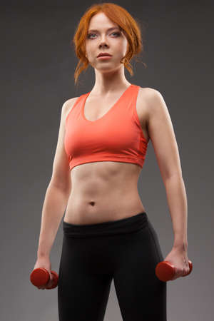 red -haired woman excersising with red dumbbells over gray backgroundの写真素材