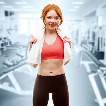 red-haired happy woman standing with towel over gym interiorの写真素材