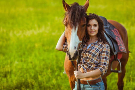 brunette cowgirl woman posing with horse outdoors portraitの写真素材