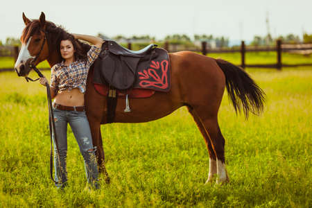brunette cowgirl woman standing with horse on fieldの写真素材