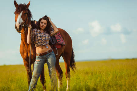 brunette cowgirl woman posing with horse outdoors portraitの写真素材