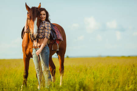 brunette cowgirl woman posing with horse outdoors portraitの写真素材