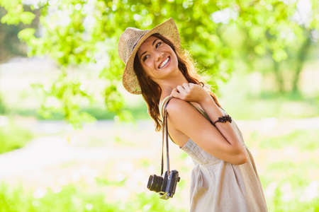 happy young girl wearing straw hat with vintage camera walking in the park and looking back, copy space from the left sideの写真素材