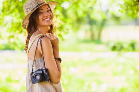happy young girl wearing straw hat with vintage camera walking in the park, copy space from the right sideの写真素材
