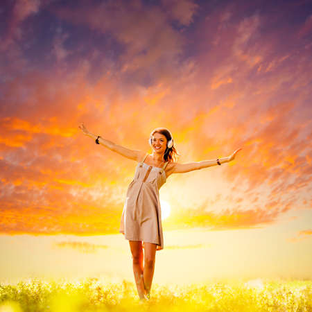 beautiful girl wearing headphones walking on sunsetの写真素材