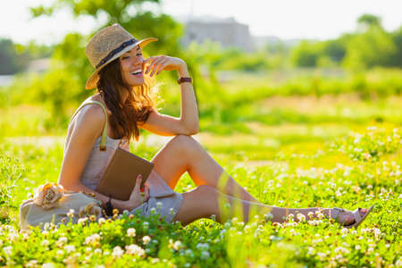 beautiful girl wearing hat with book sitting on grassの写真素材