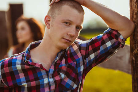 young adult couple on the farm stading near fence, man in the foreground
