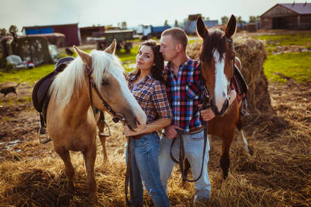 young adult couple standing on farm with horsesの写真素材