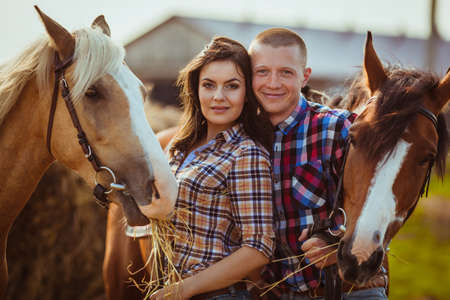 young adult couple standing on farm with horsesの写真素材