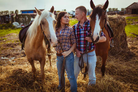 young adult couple standing on farm with horsesの写真素材