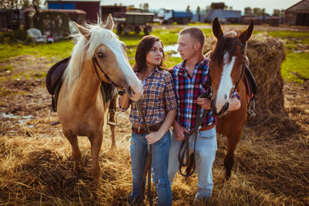 young adult couple standing on farm with horsesの写真素材