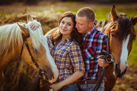 young adult couple standing on farm with horses, closeup photoの写真素材