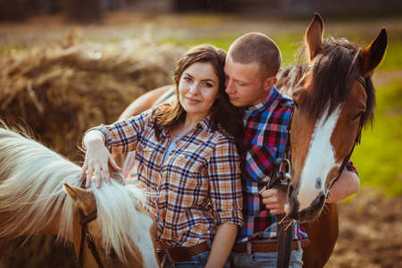 young adult couple standing on farm with horses, closeup photoの写真素材