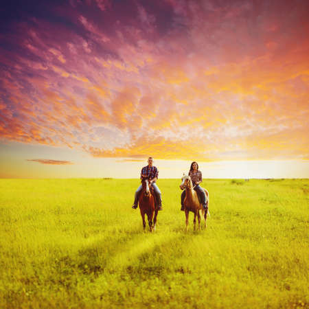 young adult copule riding on horses over sunset