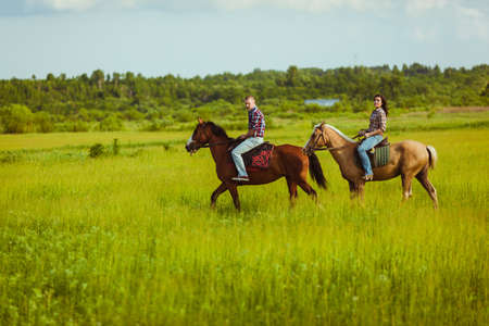 loving couple riding on horses across the green fieldの写真素材