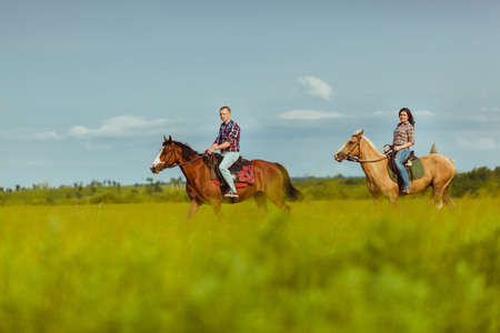 loving couple riding on horses across the field over blue skiesの写真素材