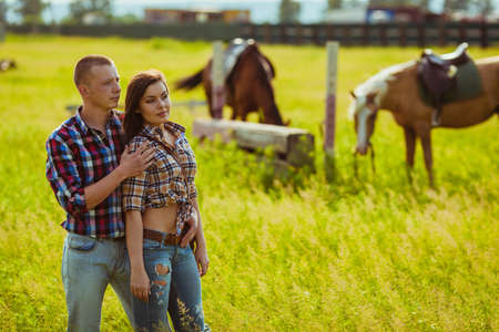 young adult cowboy style couple standing on farm with horsesの写真素材