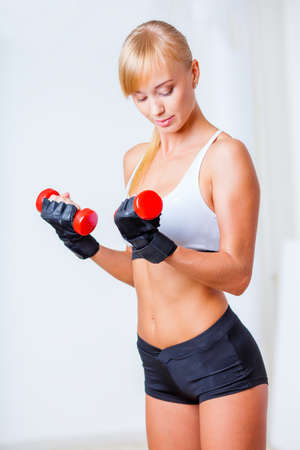 blonde sporty woman holding red dumbbells over light backgroundの写真素材