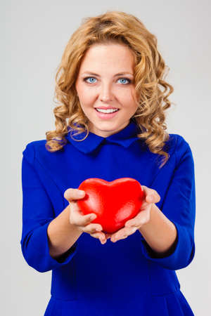 happy beautiful blonde woman wearing blue dress holding big red heartの写真素材