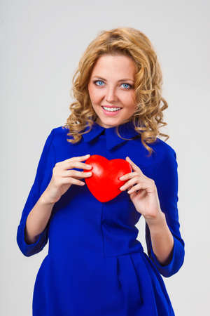 happy blonde woman wearing blue dress holding red heartの写真素材