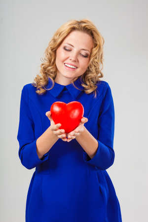 happy blonde woman wearing blue dress looking to the red heartの写真素材
