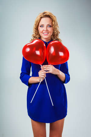 blonde woman holding red heart shaped balloonsの写真素材
