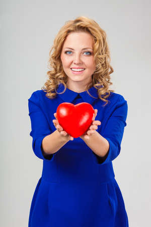 happy blonde woman wearing blue dress holding red heartの写真素材
