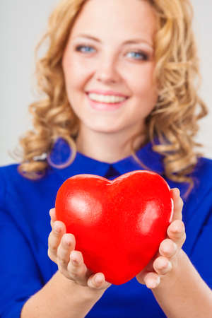 closeup photo happy blonde woman wearing blue dress holding red heartの写真素材