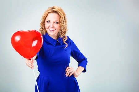 blonde woman giving to the camera red heart shaped balloonの写真素材
