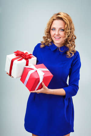 happy blonde woman wearing blue dress holding red heart and gift boxの写真素材